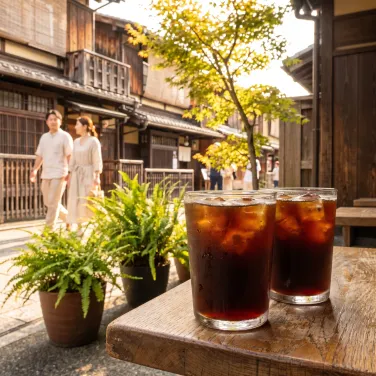 Two iced Americanos sweating on a sunlit oak table outside